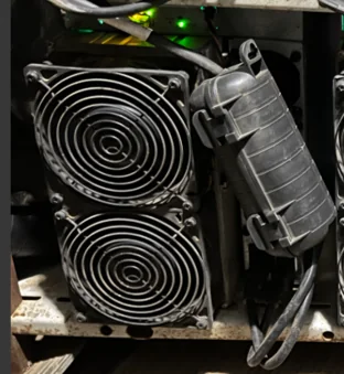 Close up of an ASIC miner in service showing two fan guards and a weatherproof power cord connector